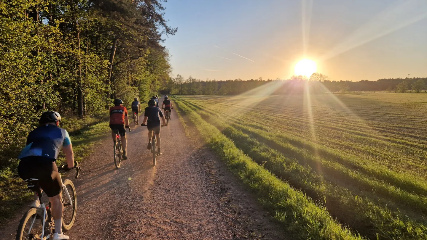 Fietsers op een gravelpad langs een veld in de ondergaande zon.