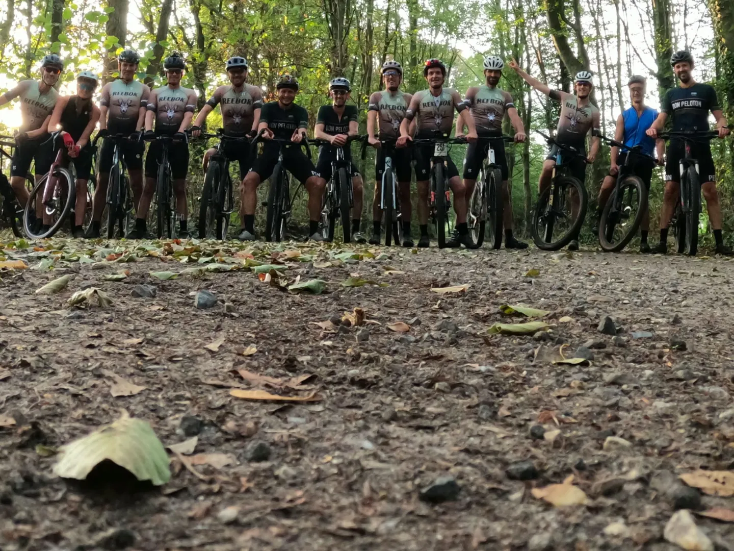 Een grote groep clubleden poseert met de fietsen tussen de bomen.