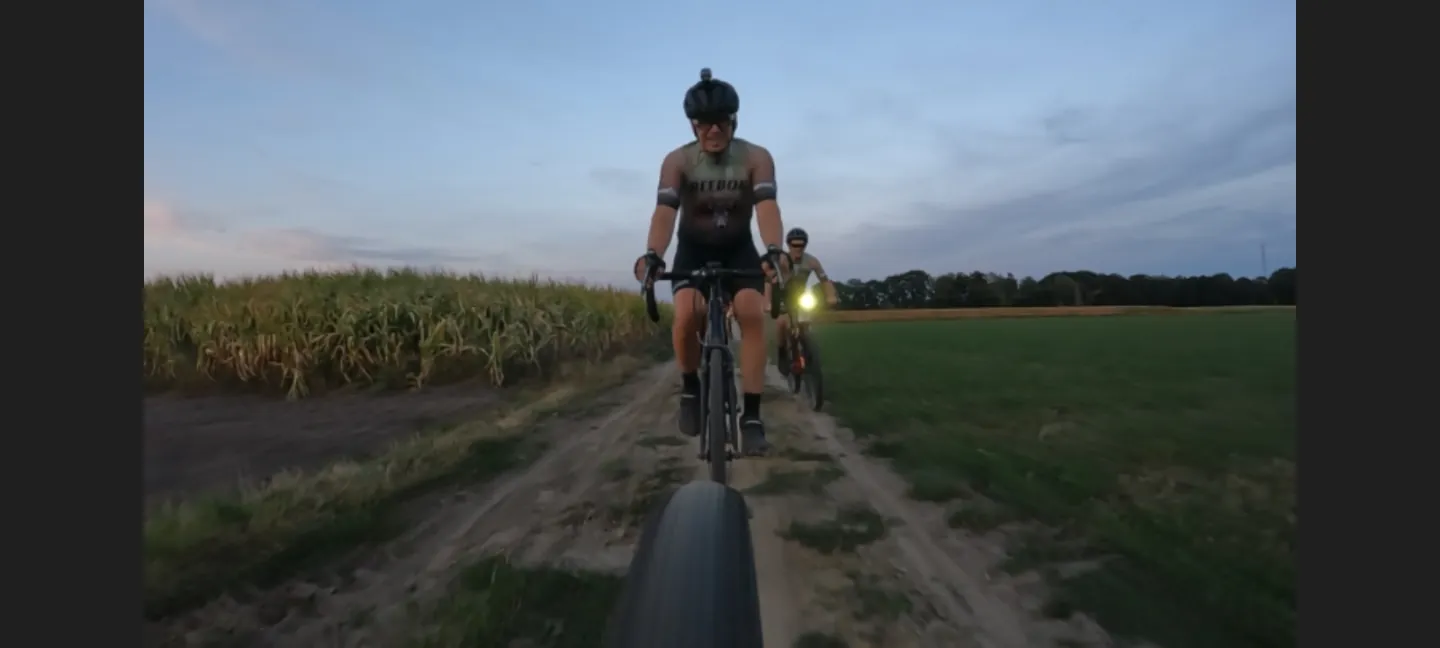Een fietser rijdt over een veldweg in de schemering.